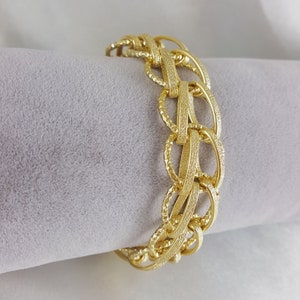 May include: A gold-colored bracelet with a textured, linked design. The bracelet features oval and rectangular links, creating a bold and stylish accessory. The metal has a matte finish, enhancing its visual appeal. This piece is suitable for various occasions.