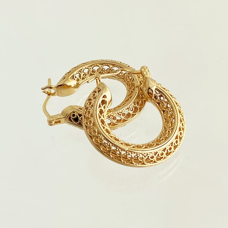 May include: Gold filigree hoop earrings with a delicate, intricate design. The earrings are lightweight and have a polished finish.