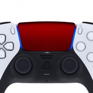 Puede incluir: Un mando de juego PlayStation 5 DualSense blanco y negro con una placa frontal roja. El mando tiene un panel táctil negro con el logotipo de PlayStation y dos botones negros a cada lado del panel táctil.