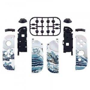Peut inclure: Un ensemble de pi&egrave;ces de rechange pour une manette Nintendo Switch. L'ensemble comprend deux panneaux lat&eacute;raux avec un motif de vague bleu et blanc, deux boutons noirs, deux joysticks noirs et une face avant noire. Les pi&egrave;ces sont emball&eacute;es dans un plateau en plastique transparent.