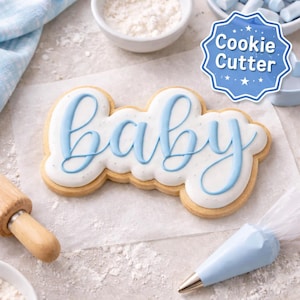May include: A frosted sugar cookie in the shape of the word "baby" with light blue icing. The cookie is on parchment paper, with a rolling pin, bowls of flour, and a piping bag in the background. A blue "Cookie Cutter" logo is in the top right.