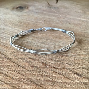 May include: A silver bracelet made from guitar strings. The bracelet is made of multiple strands of wire that are woven together.