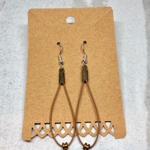 May include: A pair of dangle earrings with a teardrop shape. The earrings are made of brown wire and have a brass finish. The earrings are hanging on a brown card.