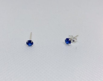 May include: A pair of silver stud earrings with small, round, blue gemstones.