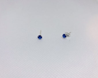 May include: A pair of silver stud earrings with small, round, blue gemstones.