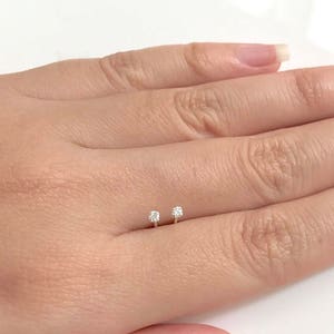 Puede incluir: Un par de pequeños pendientes de botón de plata con un solo diamante transparente en cada botón.