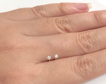 Può includere: Un paio di piccoli orecchini a perno d'argento con un singolo diamante trasparente su ogni perno.