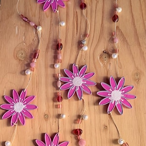 May include: A pink and white floral garland with pink and white beads. The garland is made of wood and string.