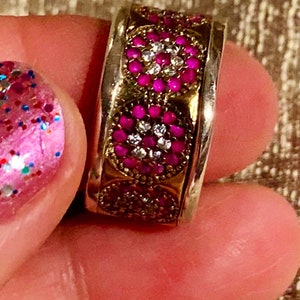 May include: A silver and gold ring with three circular designs set with pink and white stones.