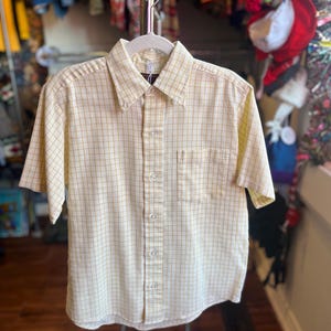 May include: A yellow and brown plaid short-sleeved button-down shirt with a pocket on the left side.