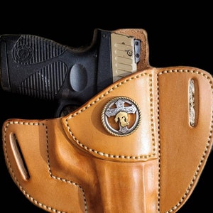 May include: A tan leather holster with a decorative metal buckle. A black and silver handgun is partially visible inside the holster.