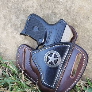 Op de afbeelding: Een bruine leren holster met een zilveren sterontwerp en een zwart pistool erin.