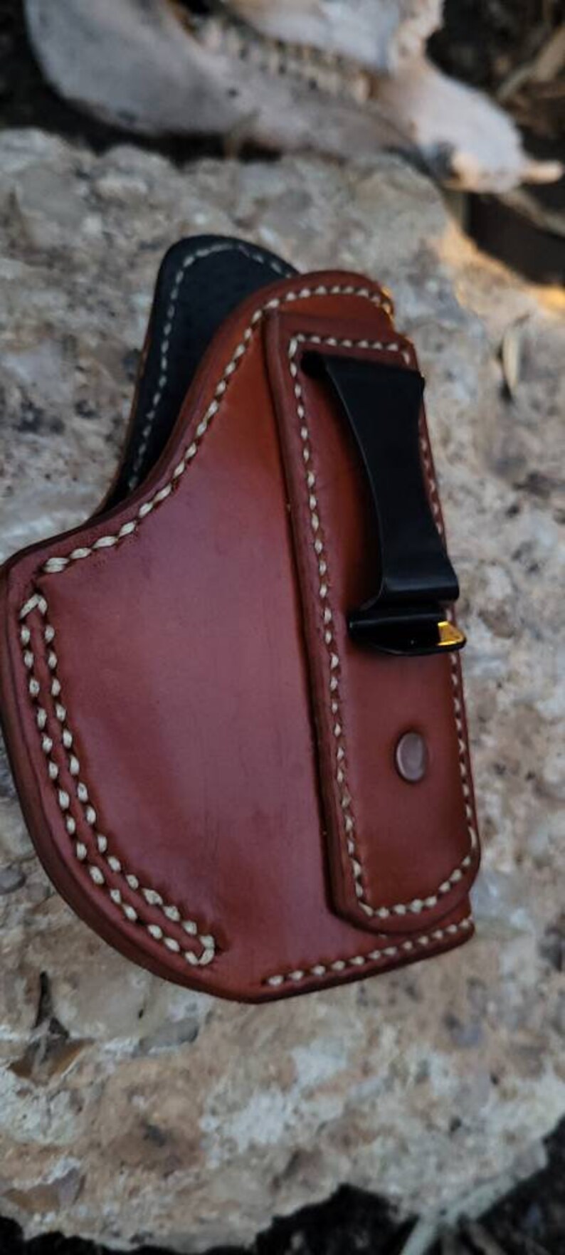 Puede incluir: Una funda de cuero marr&oacute;n con detalles de costura blanca y un clip de metal negro. La funda est&aacute; dise&ntilde;ada para sostener un arma de fuego.