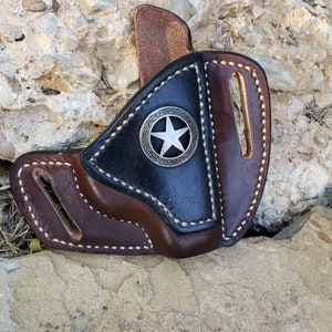 Op de afbeelding: Een bruine en zwarte leren holster met een zilveren sterontwerp. De holster is gemaakt van hoogwaardig leer en heeft een gestikt ontwerp.