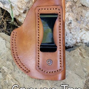 Puede incluir: Una funda de cuero marr&oacute;n con un clip negro y costuras. La funda est&aacute; etiquetada como "Canyon Tan".
