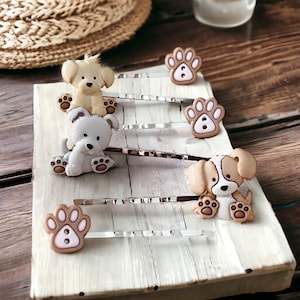 May include: Four silver hair clips with cute dog charms. The charms are brown and white with pink accents. The charms are shaped like dogs with paw prints.
