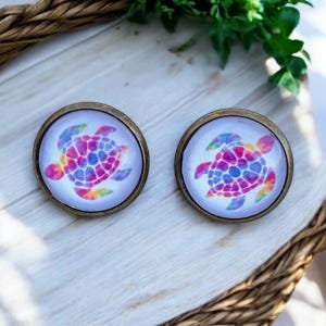 May include: A pair of round, bronze-colored earrings with a white background and a colorful tie-dye sea turtle design.