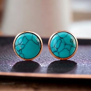 May include: A pair of turquoise and gold stud earrings. The earrings are round and have a smooth, polished finish.