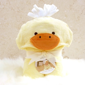 Peut inclure: Une serviette &agrave; capuche jaune avec un visage de canard et une cr&ecirc;te blanche et moelleuse. La serviette est envelopp&eacute;e et nou&eacute;e avec un ruban blanc. L'&eacute;tiquette indique "Serviette de bain enveloppante pour b&eacute;b&eacute;".