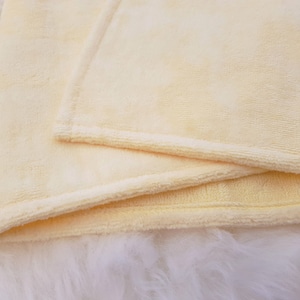 Peut inclure: Une couverture douce de couleur jaune p&acirc;le avec un bord pli&eacute;. La couverture est faite d'un mat&eacute;riau pelucheux et velout&eacute;.