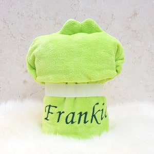 Puede incluir: Una toalla con capucha de color verde lima con una cinta blanca y el nombre "Frankie" bordado en negro.