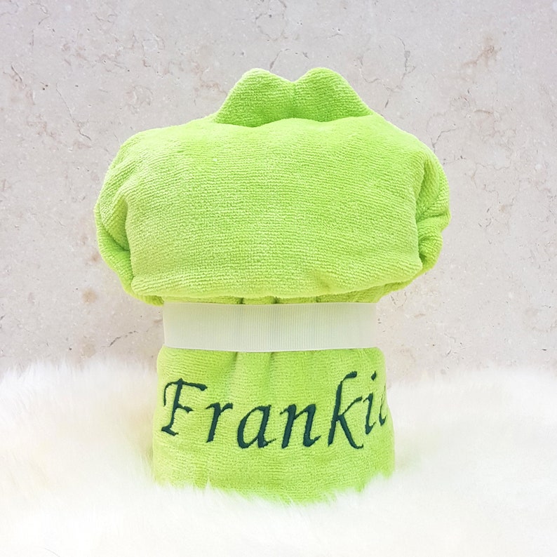 Puede incluir: Una toalla con capucha de color verde lima con una cinta blanca y el nombre "Frankie" bordado en negro.