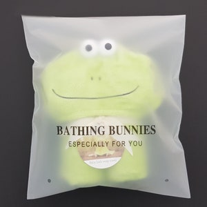 Puede incluir: Una toalla envolvente para ba&ntilde;o de beb&eacute; en forma de rana verde con el texto "Bathing Bunnies Especially For You" y "Baby bath wrap towel" impreso en ella.