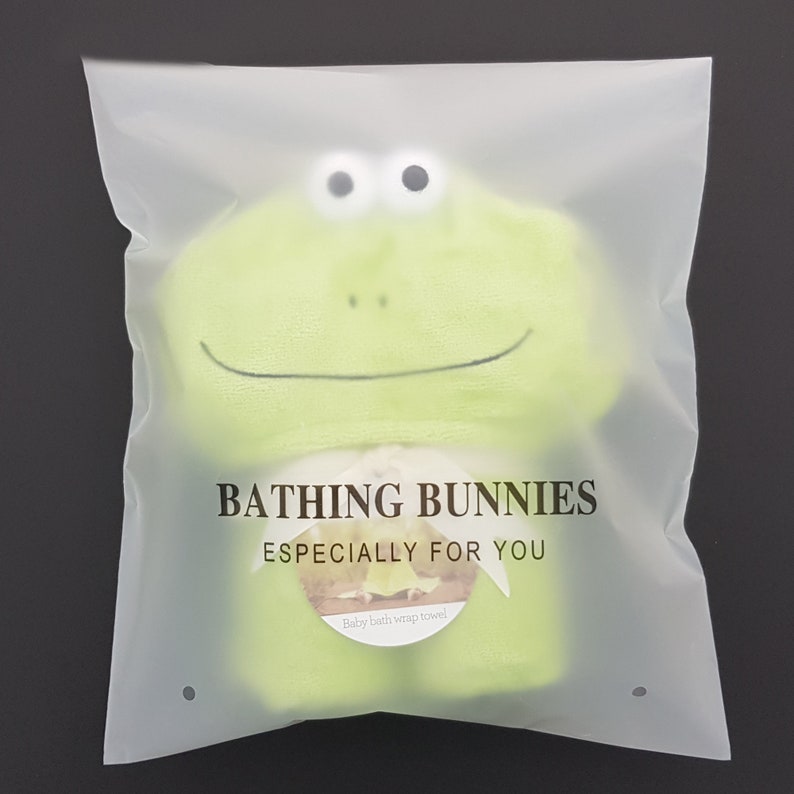 Puede incluir: Una toalla envolvente para ba&ntilde;o de beb&eacute; en forma de rana verde con el texto "Bathing Bunnies Especially For You" y "Baby bath wrap towel" impreso en ella.