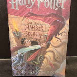 May include: A hardcover book titled "Harry Potter and the Chamber of Secrets" with a vibrant cover illustration. The cover features Harry Potter, a phoenix, and the title text in a stylized font. The author's name, J.K. Rowling, is at the bottom.