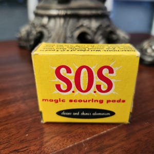 May include: A yellow box of S.O.S. magic scouring pads. The box has red text that reads "S.O.S." with "magic scouring pads" below. The bottom of the box reads "cleans and shines aluminum".