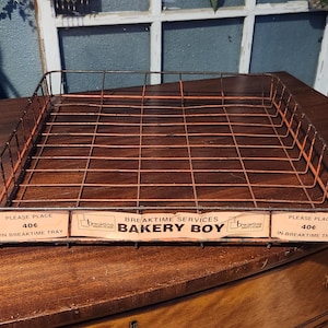 May include: A black wire bakery tray with a pink and white label that reads "Breaktime Services Bakery Boy" and "Please Place 40¢ in Breaktime Tray".