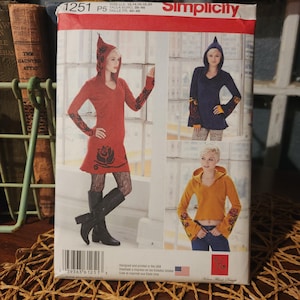 May include: Simplicity sewing pattern featuring hooded dresses and tops. The pattern includes multiple views in red, navy blue, and yellow. The pattern number is 1251, and the size range is 12-20. The package has the American flag.