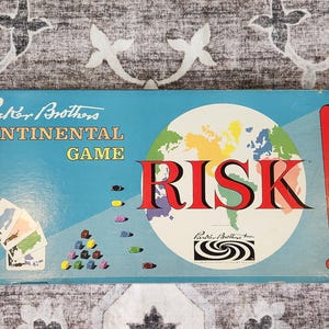 May include: A vintage "Risk" board game box. The box is light blue with the words "Parker Brothers CONTINENTAL GAME" at the top. The word "RISK" is in large red letters. A world map graphic is in the center.