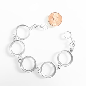May include: Silver-toned bracelet featuring six open circles linked together with small chain segments. A penny is placed next to the bracelet for size comparison. The bracelet has a lobster clasp closure.