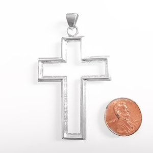 May include: A silver-colored pendant in the shape of a cross. The cross is hollow in the center and has a loop at the top for a chain. A penny is next to the pendant for size comparison.