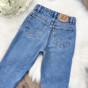 Op de afbeelding: Lichtblauwe denim jeans met klassieke vijf-zakken styling. Voorzien van een bruin leren Levi Strauss & Co. patch op de achterste tailleband en een oranje label. De jeans hebben een rechte pijp.