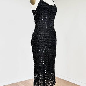 May include: A black sequined dress with spaghetti straps, displayed on a mannequin. The dress is knee-length and features a fitted silhouette. The sequins are evenly spaced, creating a shimmering effect. The dress is suitable for formal events.