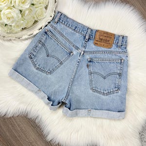 Puede incluir: Shorts vaqueros azul claro con dobladillos vueltos. Los shorts presentan un diseño clásico de cinco bolsillos, una etiqueta Levi Strauss & Co. y las costuras arqueadas icónicas de Levi's en los bolsillos traseros. Estilo vintage.