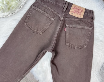 Może przedstawiać: Brązowe jeansy Levi's 501 z wysokim stanem, dwiema tylnymi kieszeniami i beżową skórzaną naszywką w pasie z napisem Levi Strauss & Co. Quality Clothing 501 W29 L30. Mała czerwona metka jest przymocowana do prawej tylnej kieszeni.