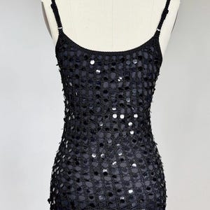 May include: Black sequin slip dress with spaghetti straps. The dress features a mesh overlay adorned with silver sequins, creating a shimmering effect. The dress is displayed on a mannequin.