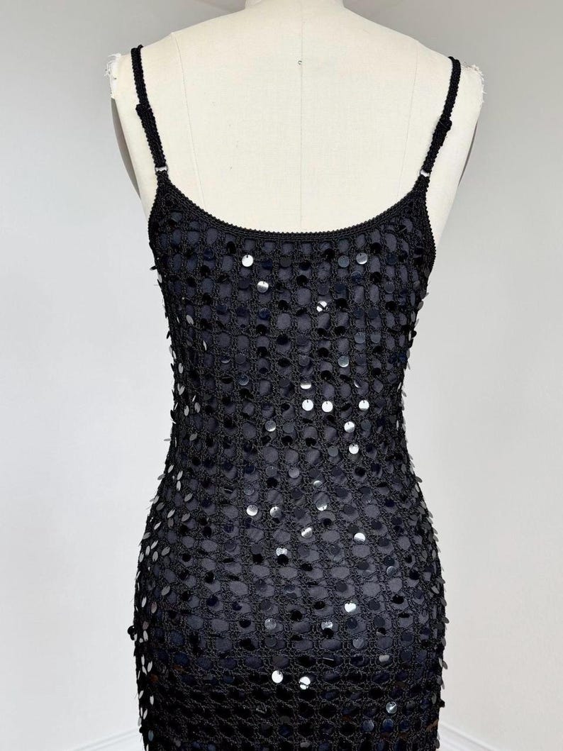 May include: Black sequin slip dress with spaghetti straps. The dress features a mesh overlay adorned with silver sequins, creating a shimmering effect. The dress is displayed on a mannequin.