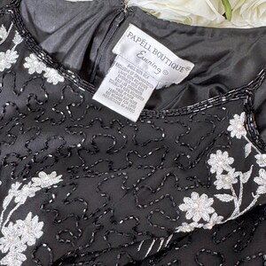 May include: Black evening dress with white floral embroidery and beaded accents. The dress features a scoop neckline and a tag that reads "PAPELL BOUTIQUE Evening". The dress is made of silk and polyester.