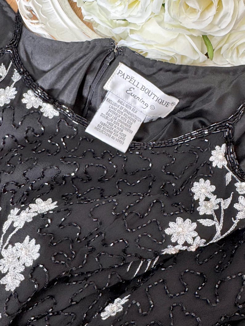 May include: Black evening dress with white floral embroidery and beaded accents. The dress features a scoop neckline and a tag that reads "PAPELL BOUTIQUE Evening". The dress is made of silk and polyester.