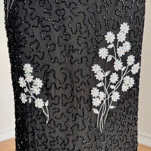 May include: Black fabric with an all-over beaded pattern and white floral embroidery. The floral embroidery is clustered in several places on the fabric. The beaded pattern is a squiggly design.