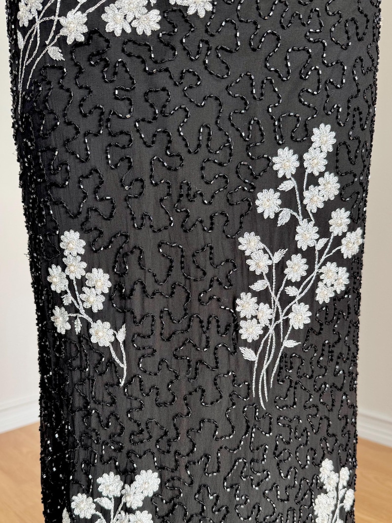 May include: Black fabric with an all-over beaded pattern and white floral embroidery. The floral embroidery is clustered in several places on the fabric. The beaded pattern is a squiggly design.