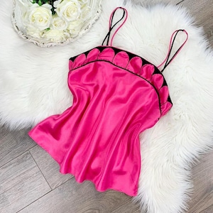 May include: A vibrant pink satin camisole with black trim and spaghetti straps. The top features a scalloped neckline and a flowing, lightweight design. The camisole is a bright, eye-catching piece.