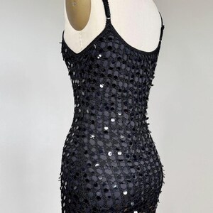 May include: Black sequined dress with spaghetti straps. The dress is displayed on a mannequin, showcasing its form-fitting silhouette. The sequins are densely packed, creating a shimmering effect. The dress appears to be made of a mesh-like material.