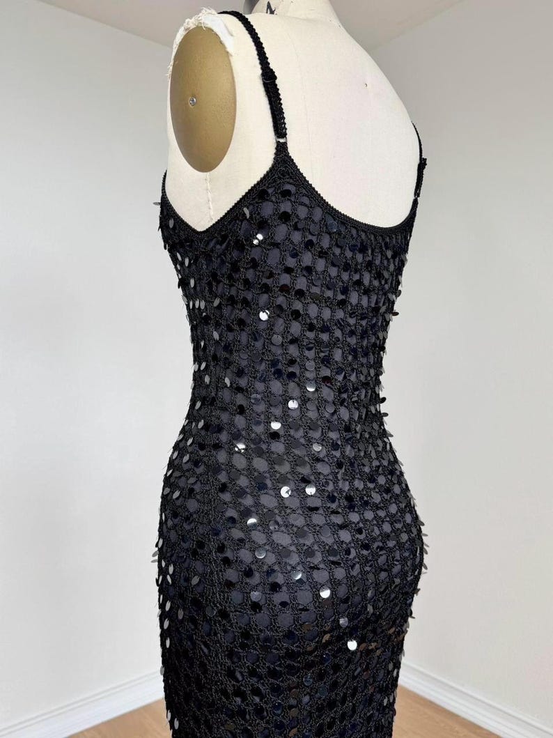May include: Black sequined dress with spaghetti straps. The dress is displayed on a mannequin, showcasing its form-fitting silhouette. The sequins are densely packed, creating a shimmering effect. The dress appears to be made of a mesh-like material.