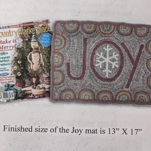 May include: A rectangular gray rug with the word "JOY" in burgundy and a white snowflake. The rug is 13" x 17". A magazine with a snowman on the cover is next to the rug.