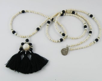 Long necklace of ivory howlite gemstone beads with black riverstone and a large pendant of cotton tassels with a Swarovski pearl centre.